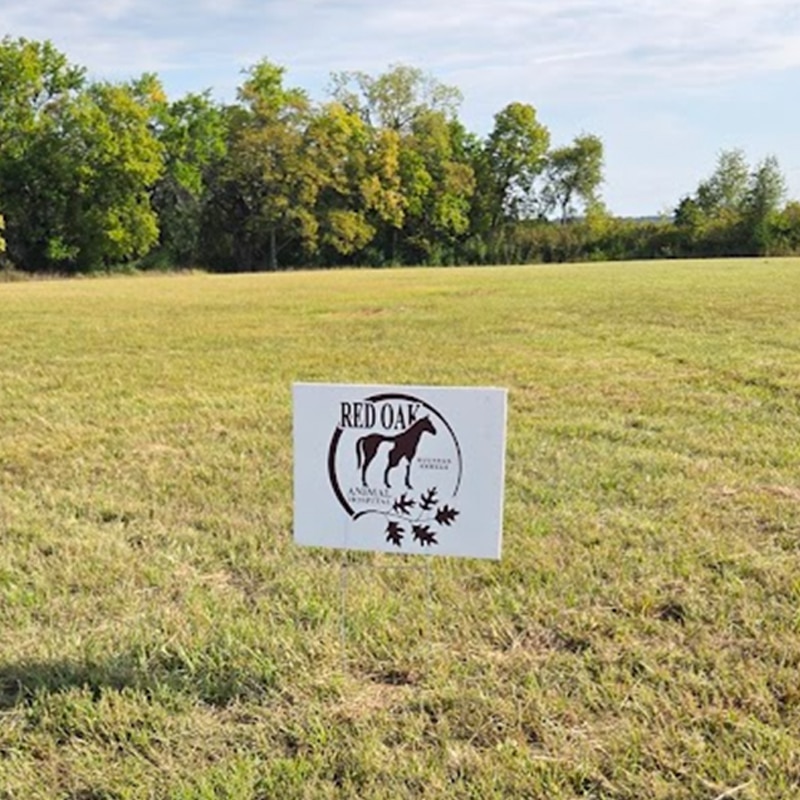 A sign on a grassy field reads "Red Oak Animal Rescue" with a horse silhouette and oak leaves in the logo. Trees and a clear sky are visible in the background.