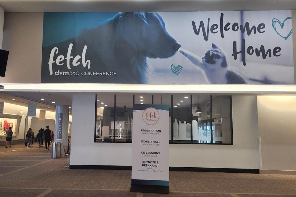 A large banner with a dog and cat says "Welcome Home" and "fetch dvm360 conference" above a hallway. Below it, a sign lists conference areas: registration, exhibit hall, CE sessions, and keynote & breakfast.
