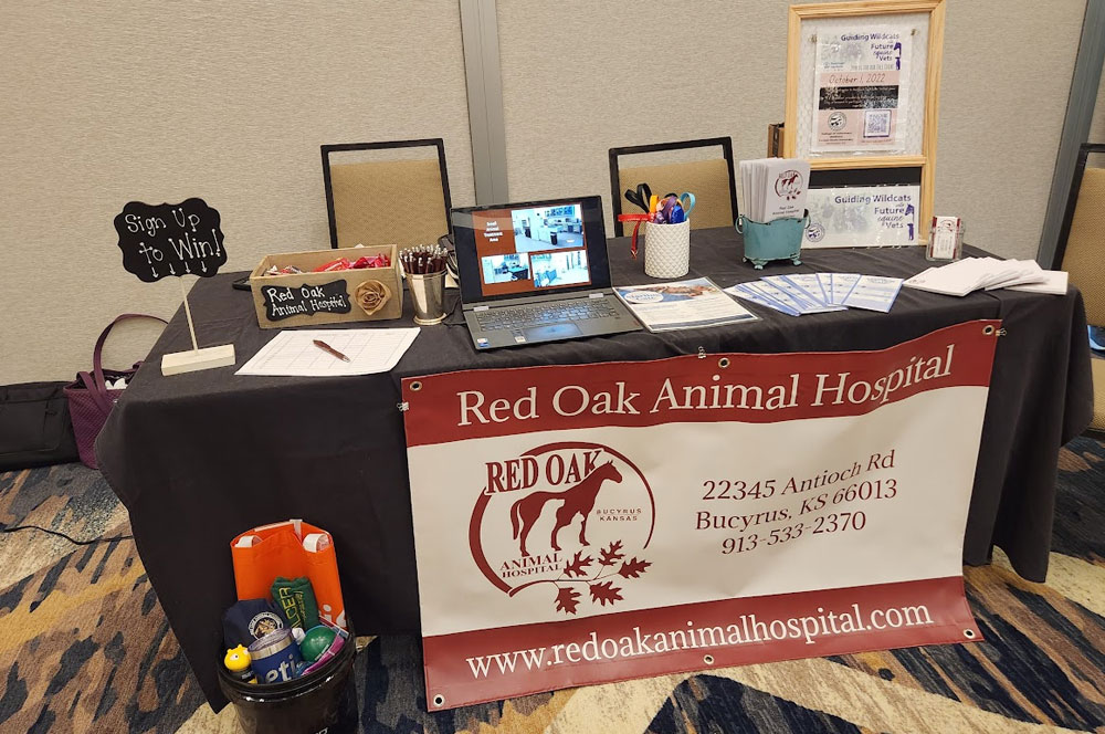 A display table for Red Oak Animal Hospital with brochures, a laptop, pens, business cards, a raffle sign, and a large banner showing the hospital's name, address, phone number, and website.